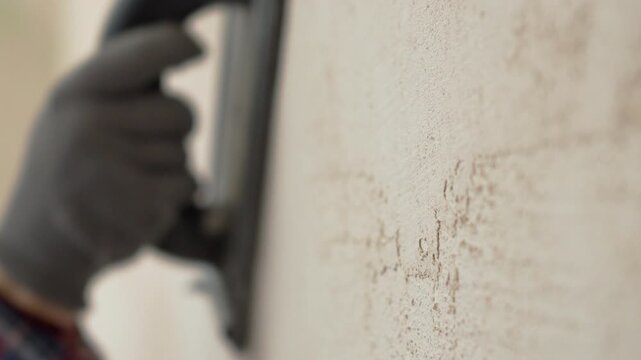 Sanding plaster wall texture with mesh tool during home renovation
