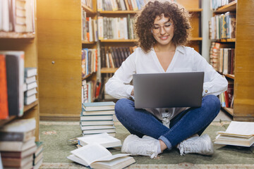 Female student learning and researching online with laptop in university library, surrounded by books and knowledge © anatoliycherkas