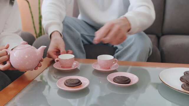 Family serving tea and cookies in pink cups while seated on a couch in a cozy living room during the afternoon hours