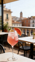 Fototapeta premium Vertical photo of a pink spritz cocktail with grapefruit and passion fruit. Refreshing summer drink on a rooftop terrace overlooking a European city. Aperitivo lifestyle concept