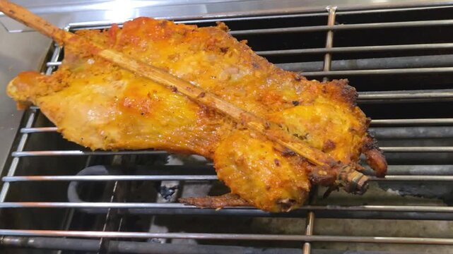 Traditional Thai grilled chicken (Gai Yang) skewered on a bamboo stick and roasting on a metal electric grill.