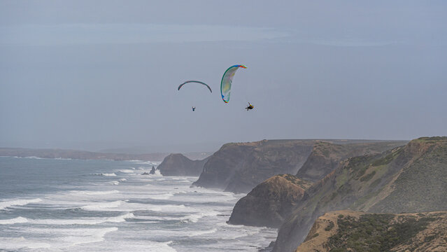 Paragliders soar above the cliffs of Cordoama, Portugal