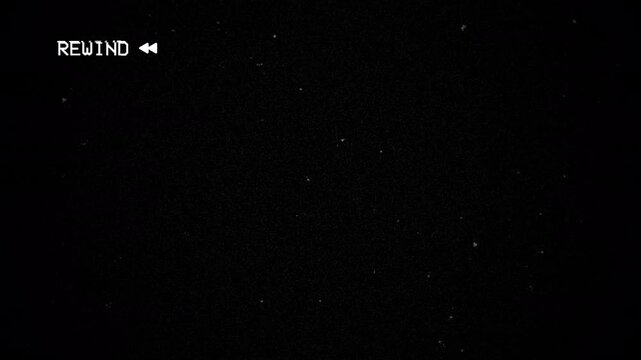 Rewind scratches enhance the grainy black screen showcasing the word rewind for a vintage aesthetic.Rewind old film grainy black video shows rewind and activate windows text resembling vintage film.