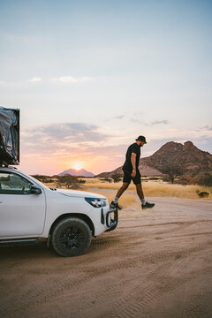 Traveler stepping from off road vehicle at sunset in Spitzkoppe