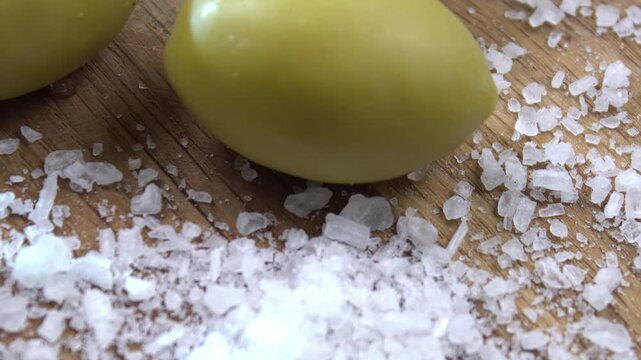 Green olives (Olea europaea) with coarse sea salt on wood, dry curing and osmosis dehydration process, Food Science Background.