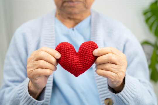 Asian elder senior woman patient holding red heart in hospital.