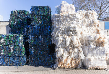 Large, rectangular bales of sorted plastic waste, including blue crates and white film, stacked for recycling