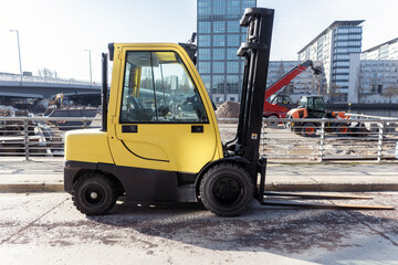 profile shot of a modern yellow forklift parked at a city construction site with modern office buildings in the background