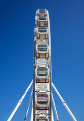 Low-angle view of a large, white modern Ferris wheel with glass gondolas against a deep blue, cloudless sky