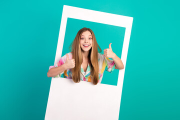 Smiling young woman in vibrant attire showing thumbs up gesture against a bright turquoise background with a trendy frame concept