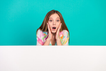 Surprised young woman with hands on face against a vibrant turquoise background, wearing a colorful shirt