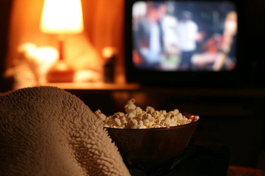Family movie night in living room with DVD menu on CRT television, popcorn bowl and fleece blankets in warm lamp glow