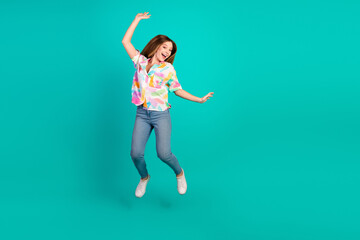 Cheerful young woman jumping in stylish attire against a vibrant teal background showcasing a...