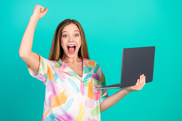 Fototapeta na wymiar Young woman with raised hand and laptop expressing happiness on a turquoise background