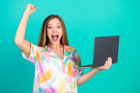 Young woman with raised hand and laptop expressing happiness on a turquoise background