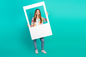 Cheerful Young Woman Holding a Photo Frame Prop Against a Vibrant Teal Background in a Casual and...