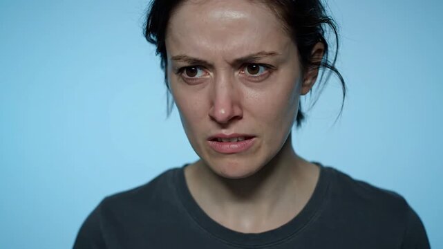 A woman displays a sequence of facial expressions, from anger to confusion, against a plain light blue background, captured in a video snippet showing multiple emotional states.