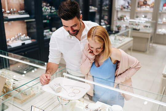 A happy young couple looks at bracelets and diamond jewelry inside a glass display case at a high-end jewelry store.