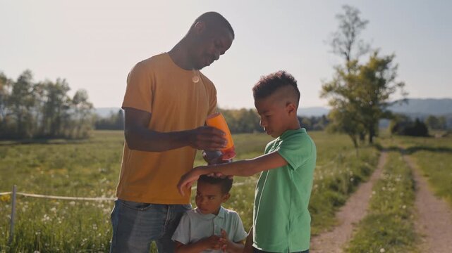 While spending time outdoors in the summer, a father applying sunscreen to his sons to keep them safe from the sun, medium shot.