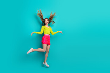 Joyful young woman jumping on a turquoise background wearing colorful casual outfits, expressing happiness and energetic vibes