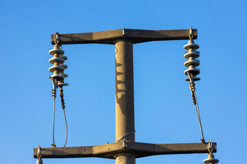 Fototapeta premium Close up of concrete electric pole with ceramic insulators against clear blue sky. High voltage power line industrial equipment in morning sunlight.