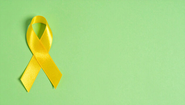Yellow awareness ribbon placed on green background, top view composition. For troops military, suicide prevention