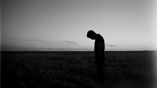 Solitary figure standing on empty prairie, bowed head facing distant horizon at dusk, grainy film texture, melancholic atmosphere, slow contemplative pace, wandering drifter