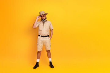 Man in safari outfit stands against a bright yellow background posing with sunglass and hat for adventure travel style and summer exploration © deagreez