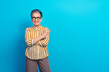 Confident aged female senior woman with striped shirt smiles warmly while pointing side ckground...