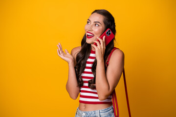 Young woman on bright yellow background chats on a red smartphone in striped casual top