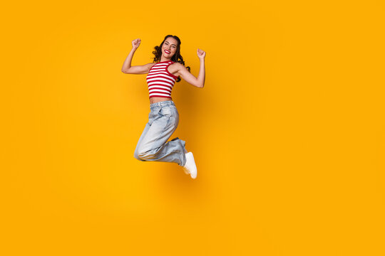 Joyful young woman jumps in striped top against bright yellow background