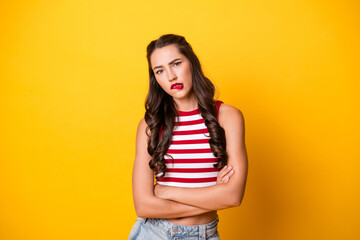 Young woman with striped red and white top stands against bright yellow background with arms crossed and serious expression © deagreez