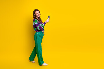 Fototapeta premium Young woman stands yellow background in sweater green pants taking selfie smiling and enjoying casual fashion moment for lifestyle advertising