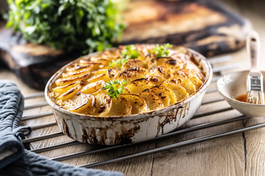 Golden-brown gratin potatoes, neatly arranged in a white ceramic bowl and garnished with fresh herbs. In Slovakia, however, this dish is known primarily at home as French potatoes
