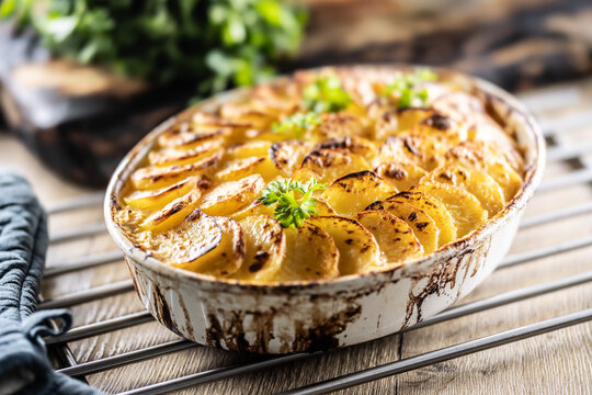 Golden-brown gratin potatoes, neatly arranged in a white ceramic bowl and garnished with fresh herbs. In Slovakia, however, this dish is known primarily at home as French potatoes