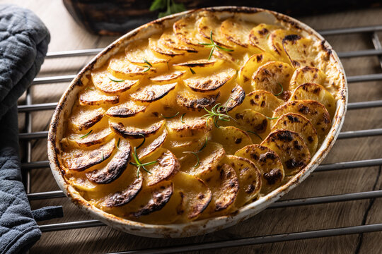Golden-brown gratin potatoes, neatly arranged in a white ceramic bowl and garnished with fresh herbs. In Slovakia, however, this dish is known primarily at home as French potatoes