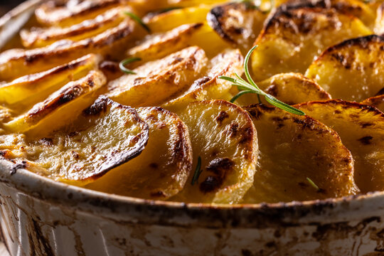 Golden-brown gratin potatoes, neatly arranged in a white ceramic bowl and garnished with fresh herbs. In Slovakia, however, this dish is known primarily at home as French potatoes