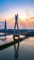 Obraz premium Tall bridge and skyscraper reflected in calm water during sunset, an aerial view