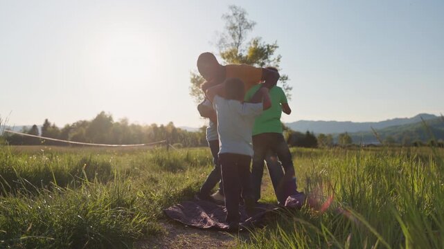 Smiling dad wrestling and playing with his kids outdoors on a sunny day, enjoying family fun in nature, handheld shot. Father-son bonding concept.