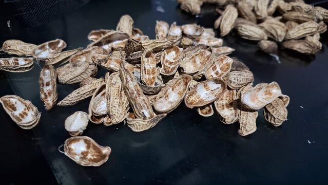 Peanut shells Arachis hypogaea scattered on dark tabletop background close up angle realistic photography macro shot of organic food waste leftovers and snack debris for composting concept