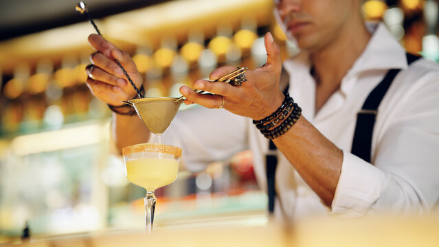 Skilled bartender accurately straining a craft cocktail into a glass, creating a perfect mixed drink for customers