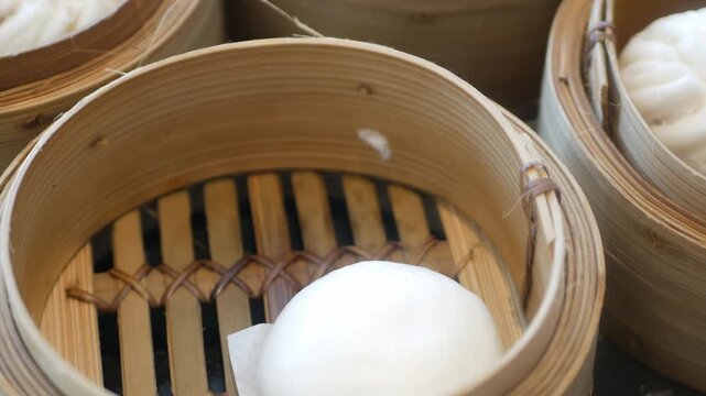 close up view to a steamer full with chinese bun dimsum in hongkong style with hot streaming while a hand pick up chinese bun from steammer,chinese dimsum food eating