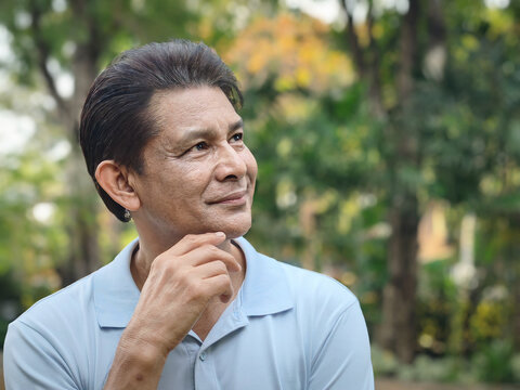 Asian senior man with white hair thinking, planning with happy positive optimistic facial expression, green city outdoor scene