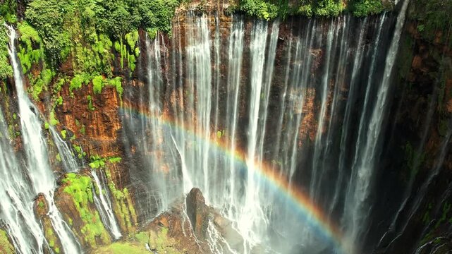 Aerial view of Tumpak Sewu massive multi stream waterfall in Java, Indonesia with rainbow over lush cliff amphitheater