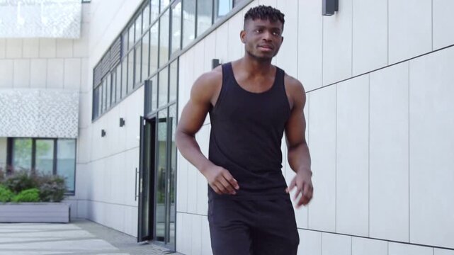 African American man runs along city street and gets tired and out of breath, athletic guy takes break during workout and catches his breath