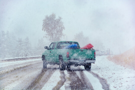 Drivers perspective view over road covered with snow and pick up truck in front slipping and sliding to brake for upcoming traffic jam during heavy snow storm