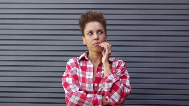 thoughtful African American woman plans and thinks against the backdrop of urban wall, unsure girl dreams and imagines solution and chooses outdoors