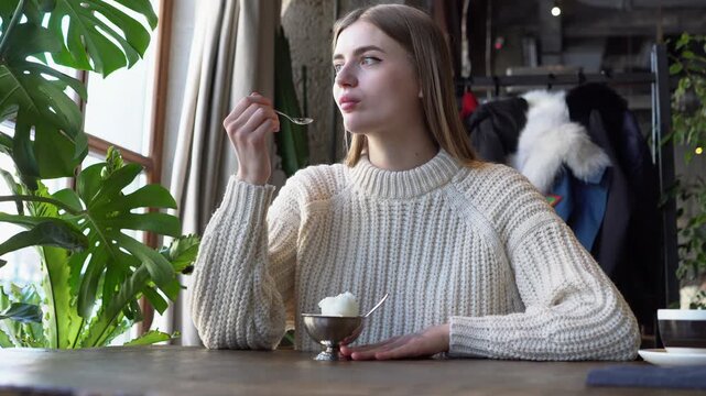 young beautiful woman eats ice cream with spoon in cafe, girl eats plombir dessert in restaurant