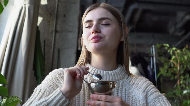 young beautiful woman eats ice cream with spoon in cafe, girl eats plombir dessert in restaurant