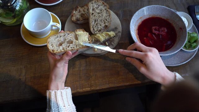 young beautiful woman spreads butter on bread in cafe, girl eats Ukrainian borscht with lard and bread in restaurant, close-up